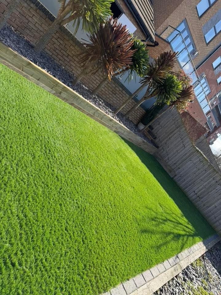 Close-up of newly laid artificial grass with slate edging along a boundary wall