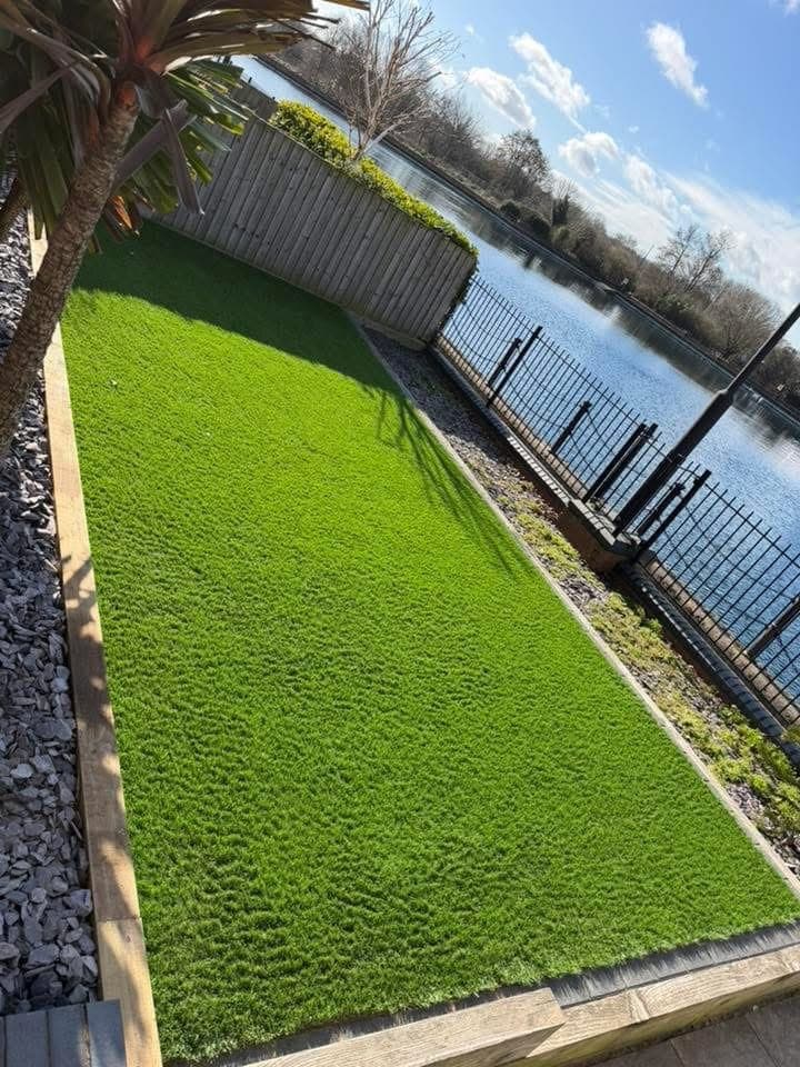 Newly laid artificial lawn edged with slate chippings, beside a fence and railings