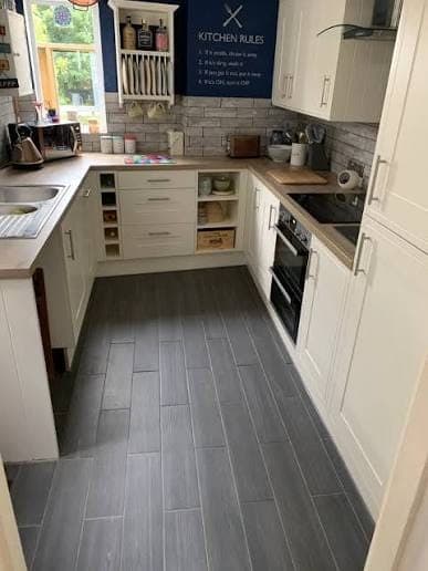 Cream shaker-style kitchen with wood-effect worktops, a brick-effect splashback and grey wood-effect flooring