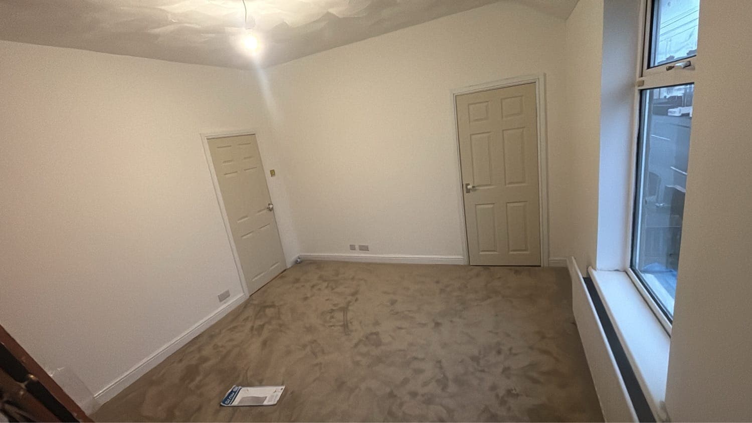 Empty room repainted in white with two newly painted doors and beige carpet