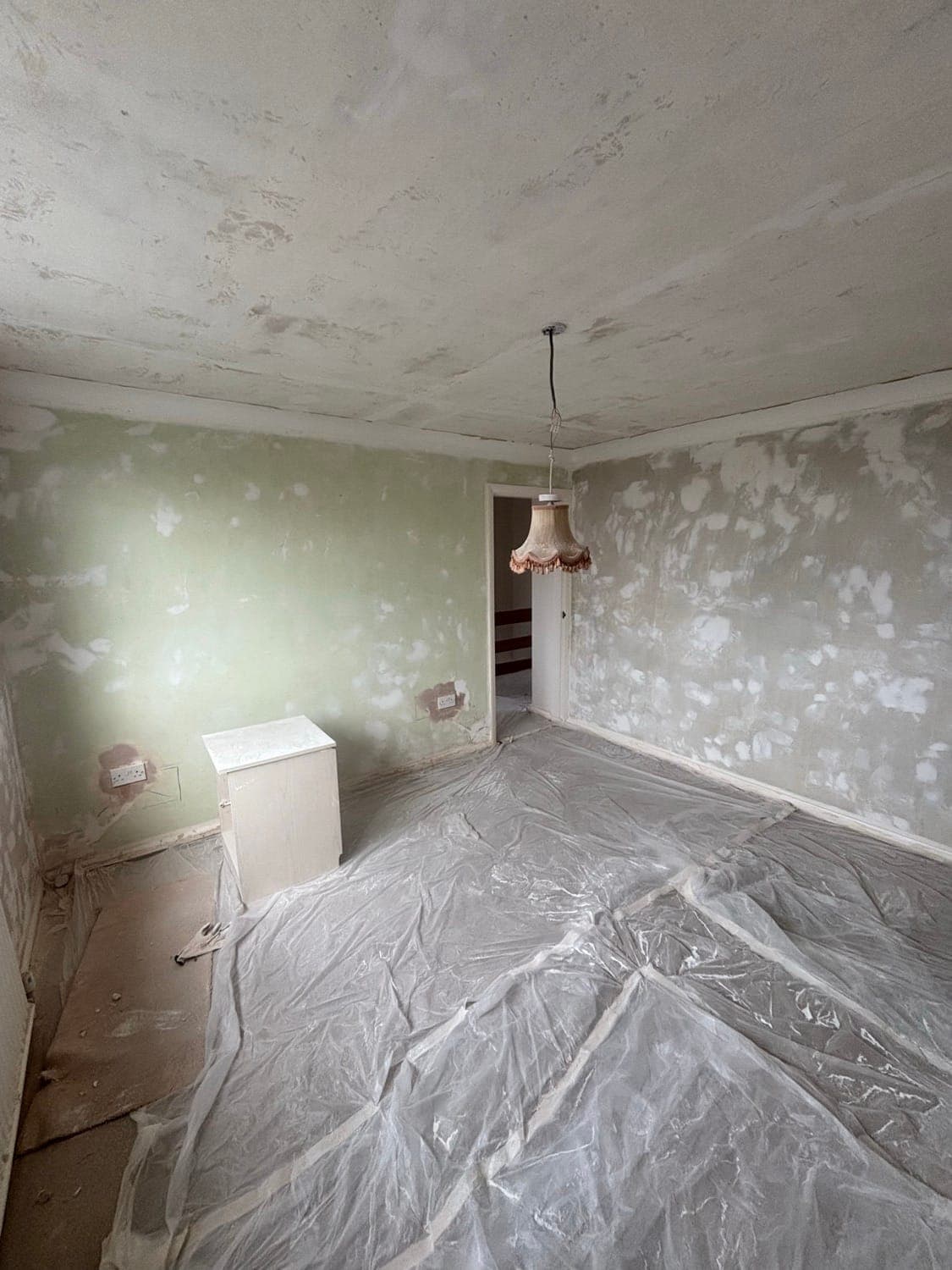 Living room stripped of wallpaper with the walls filled and dust sheets down, before skimming and decorating