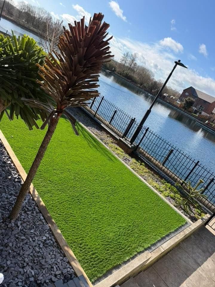 Artificial grass laid in a lakeside garden with slate borders and a palm beside black railings