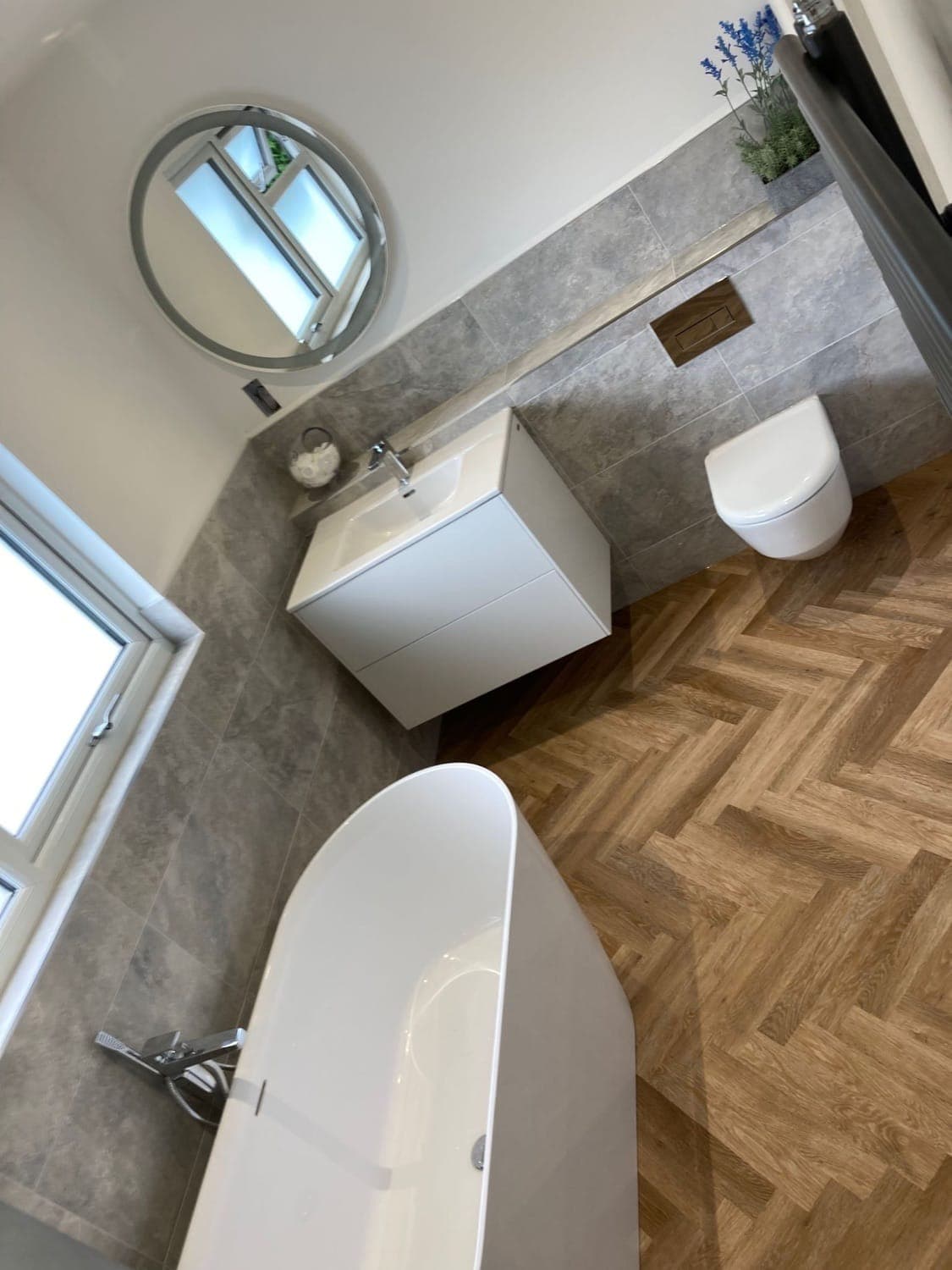 Bathroom with a herringbone wood-effect floor, wall-hung vanity basin, freestanding bath and a round mirror