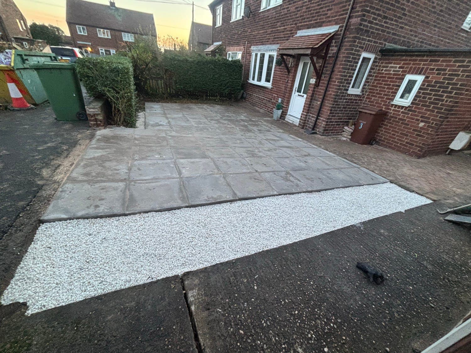 Newly paved driveway with large slabs and white gravel edging in front of a brick house