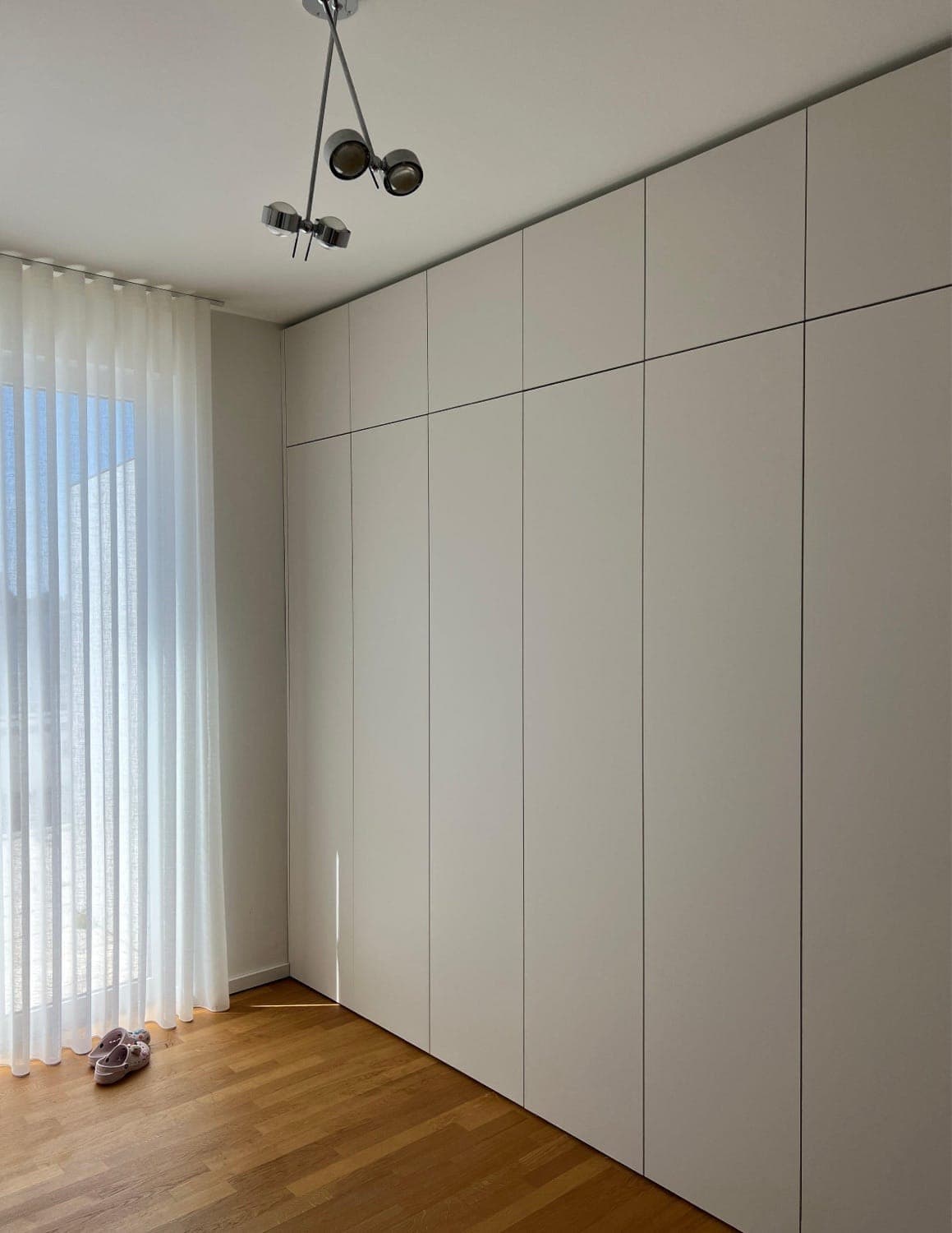 Floor-to-ceiling fitted wardrobes with white handleless doors beside a window