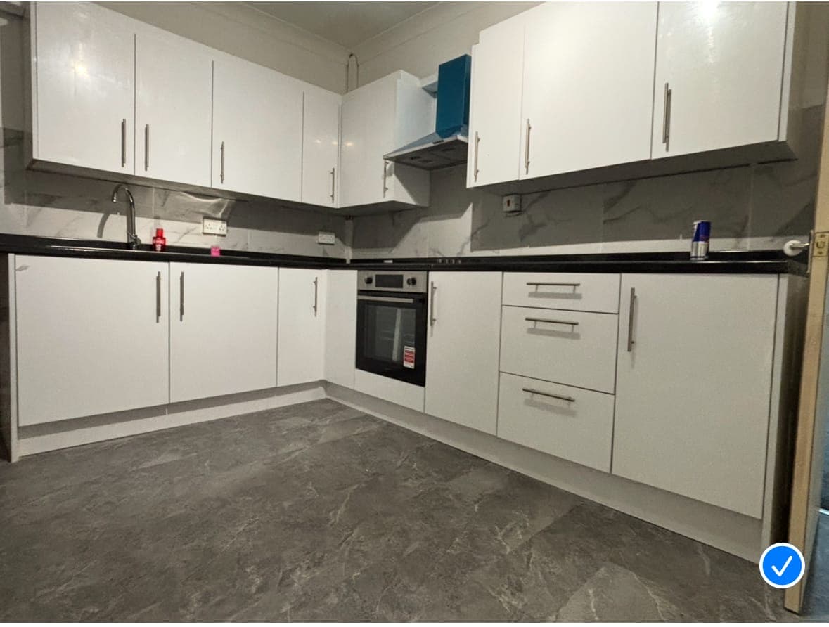 Fitted kitchen with white gloss units, black worktops, a built-in oven and grey stone-effect flooring